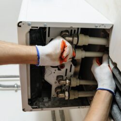 Installation of home heating. A worker attaches the pipe to the gas boiler.